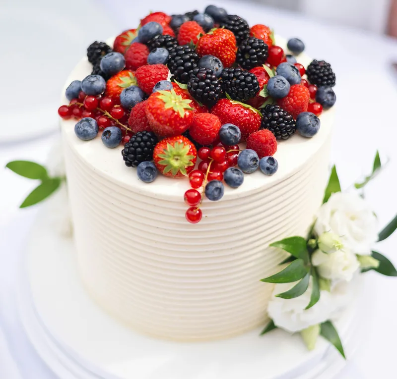 Weiße Torte mit Erdbeeren, Brombeeren, Heidelbeeren und Johannisbeeren, daneben weiße Blüten