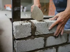 Ein Maurer setzt den nächsten Stein ins Mörtelbett, die Kelle in der anderen Hand.