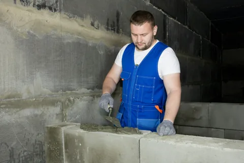 Ein Maurer setzt einen Kalksandstein mit Mörtel an einer Hauswand.