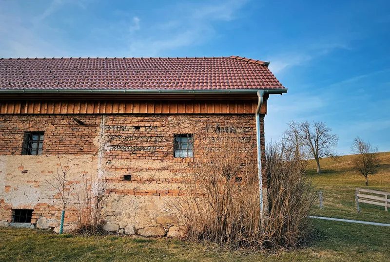 Alte Scheune aus Backstein und Feldstein mit rotem Ziegeldach und Rinne, davor eine Wiese.