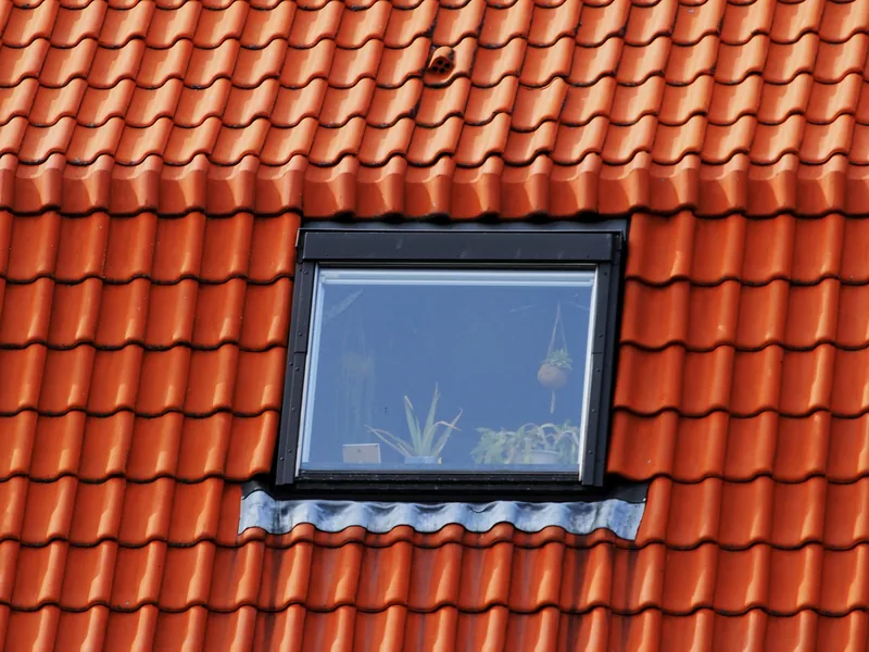 Neu eingebautes Dachfenster mit dunklem Eindeckrahmen in einem roten Ziegeldach.
