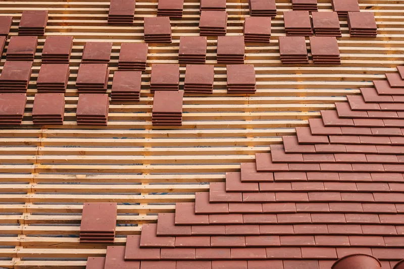 Dach im Umbau: unten schon neue rote Ziegel, oben frische Holzlatten mit kleinen Ziegelstapeln.