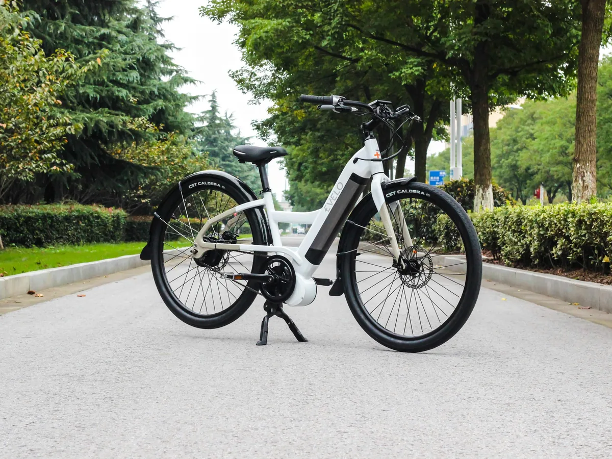 Weißes City-E-Bike mit Mittelmotor und tiefem Einstieg auf einer Allee.
