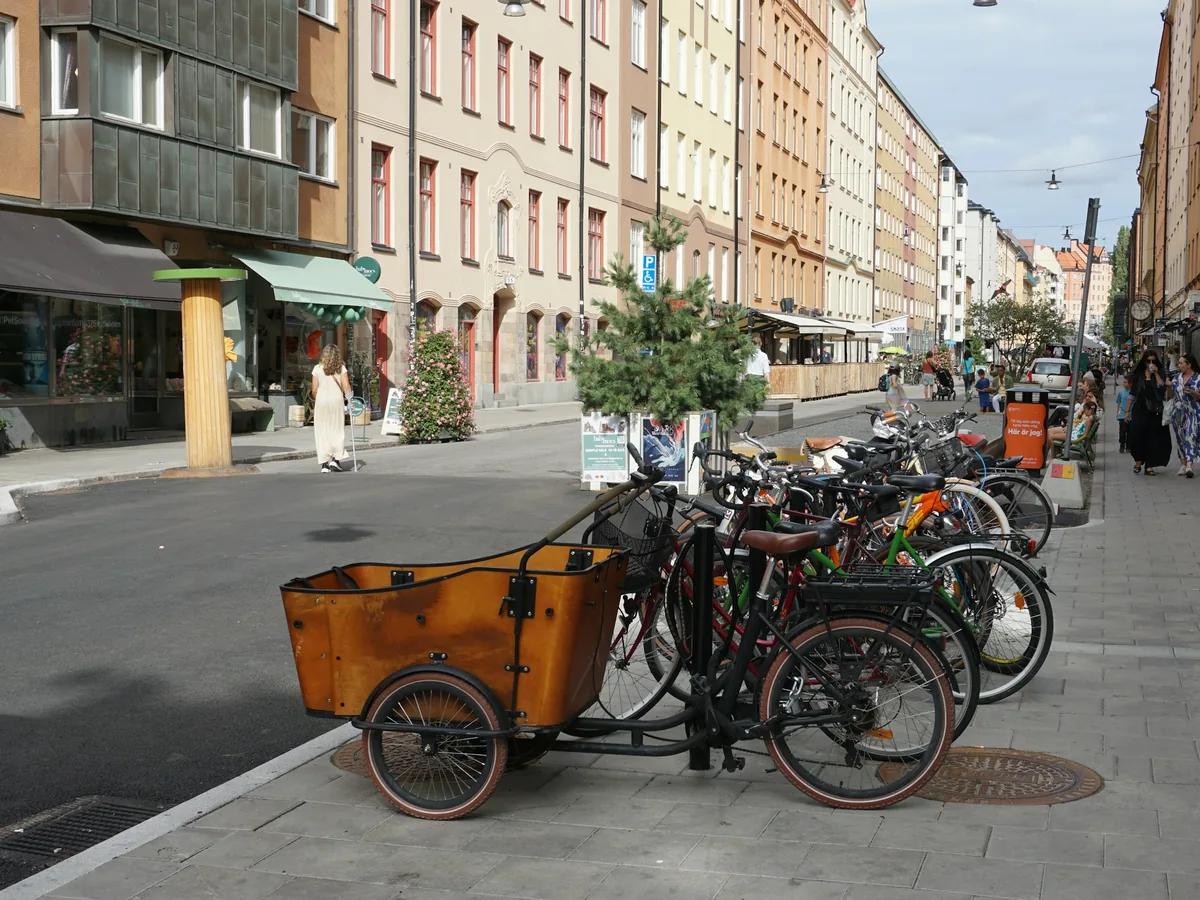 Lastenrad mit Holzkiste vorn, an einer Stadtstraße neben anderen Rädern geparkt.