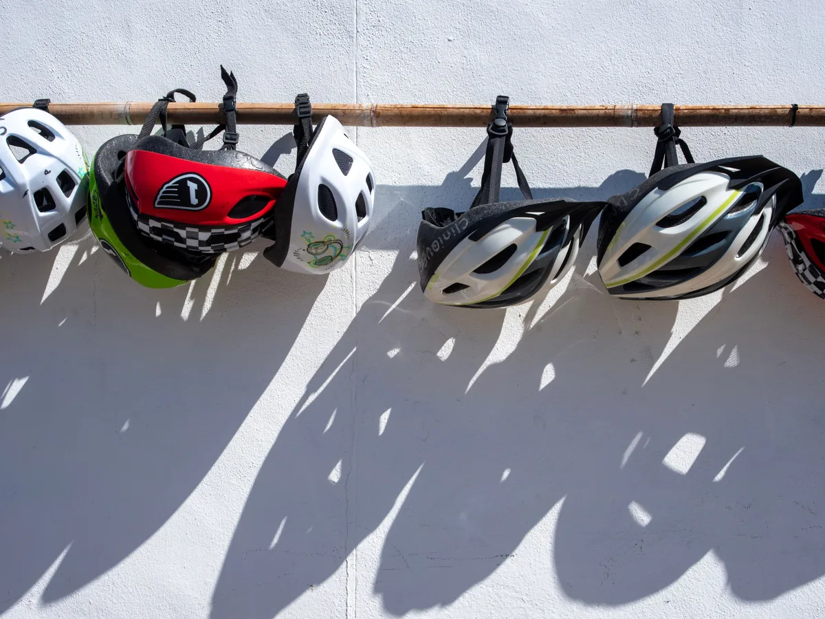 Fahrradhelme hängen an einer Stange vor einer hellen Wand.