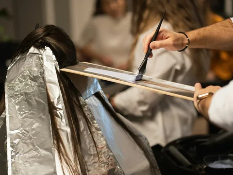 Eine Haarsträhne liegt auf einem Brett und wird mit dem Pinsel gefärbt, die übrigen Strähnen sind in Alufolie gepackt.