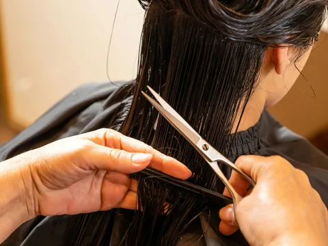 Eine Friseurin hält eine Strähne des nassen, dunklen Haares mit Kamm und Fingern fest und schneidet sie mit der Schere.