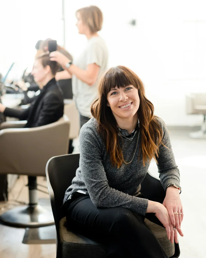 Mareike Ohlbrandt sitzt lächelnd im hellen Salon, hinter ihr wird an den Plätzen gearbeitet.