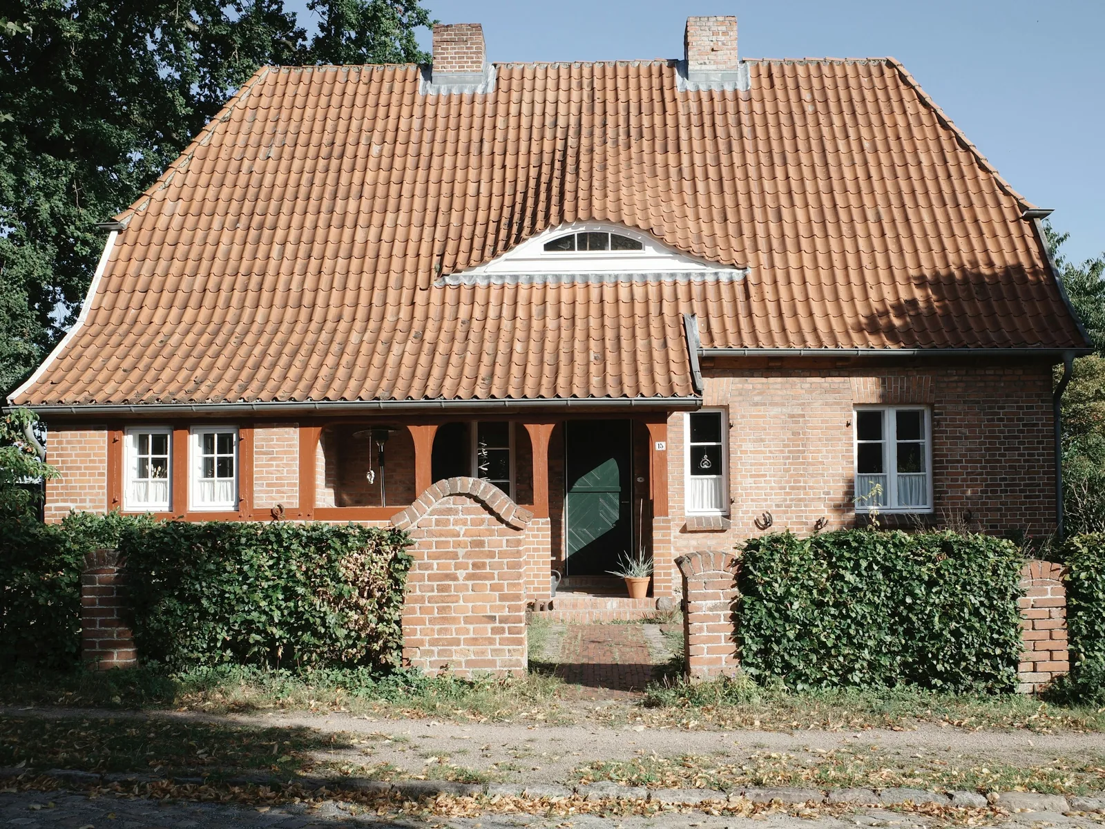 Siedlungshaus aus Backstein mit Ziegeldach und Gaube hinter einer Hecke