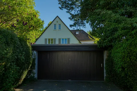 Einfamilienhaus mit Doppelgarage und gepflasterter Einfahrt zwischen hohen Bäumen
