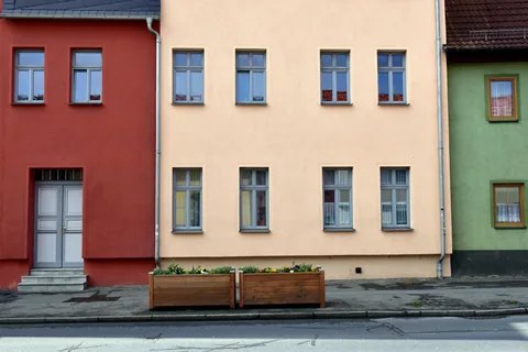 Sanierte Stadthäuser mit roter, heller und grüner Putzfassade und Blumenkästen