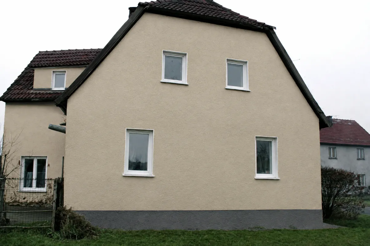 Siedlungshaus in Tiefensee nachher: Fassade in hellem Sandton, Sockel grau, Fenster weiß.