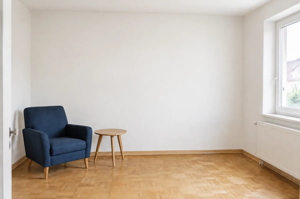 Das Wohnzimmer in Laußig nachher: glatte, frisch gestrichene Wände, blauer Sessel, Beistelltisch, Parkett, Fenster rechts.